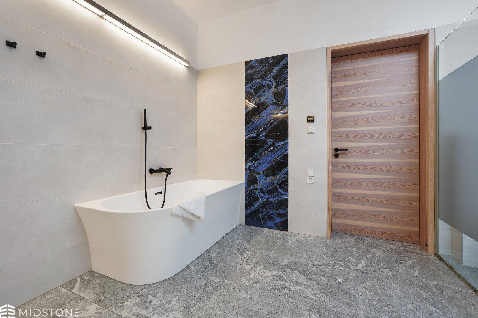 Elegantes Badezimmer mit freistehender Badewanne, modernen Fliesen und Holztür.