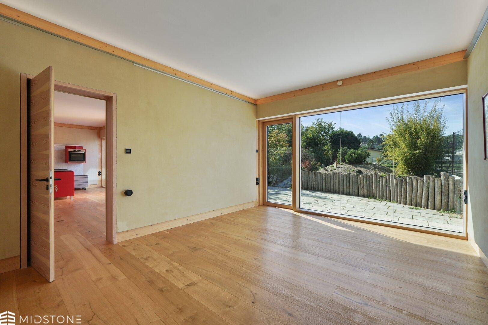 Heller Wohnbereich mit Holzboden und großen Fenstern, die den Blick auf die Terrasse freigeben.