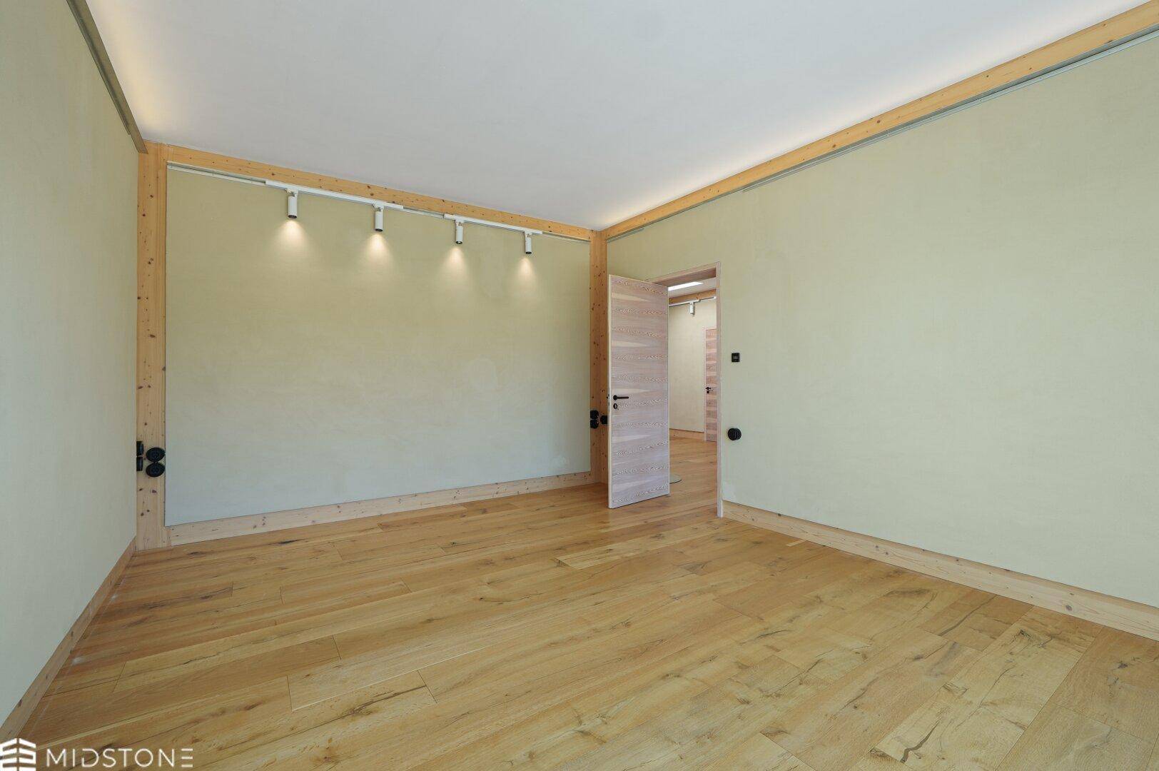 Geräumiger, heller Raum mit Holzboden und Holztür, bietet vielfältige Nutzungsmöglichkeiten.