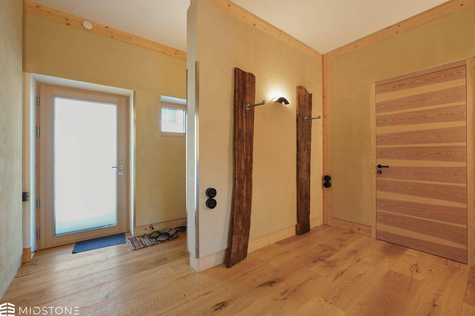 Eingangsbereich mit Holzboden, Glastür und rustikalen Holzelementen, die Charakter verleihen.
