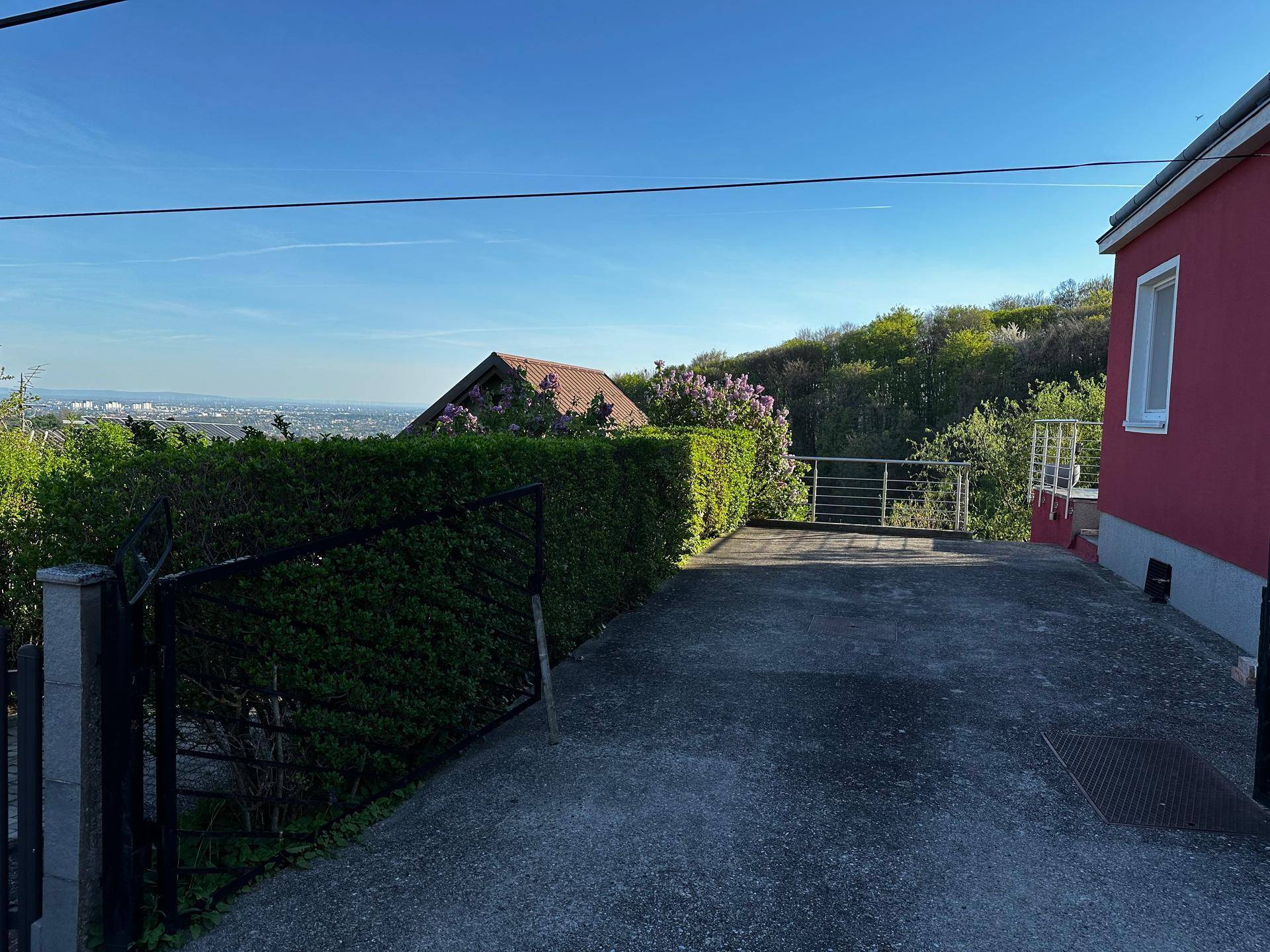 Einfahrt zum Grundstück mit Hecke und Blick auf die umliegende Landschaft.