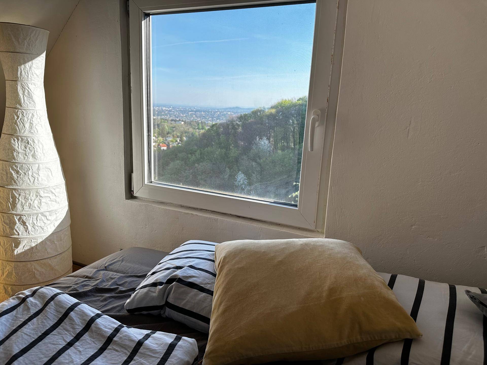 Fenster im Schlafzimmer mit weitem Blick über die grüne Landschaft und die Stadt.