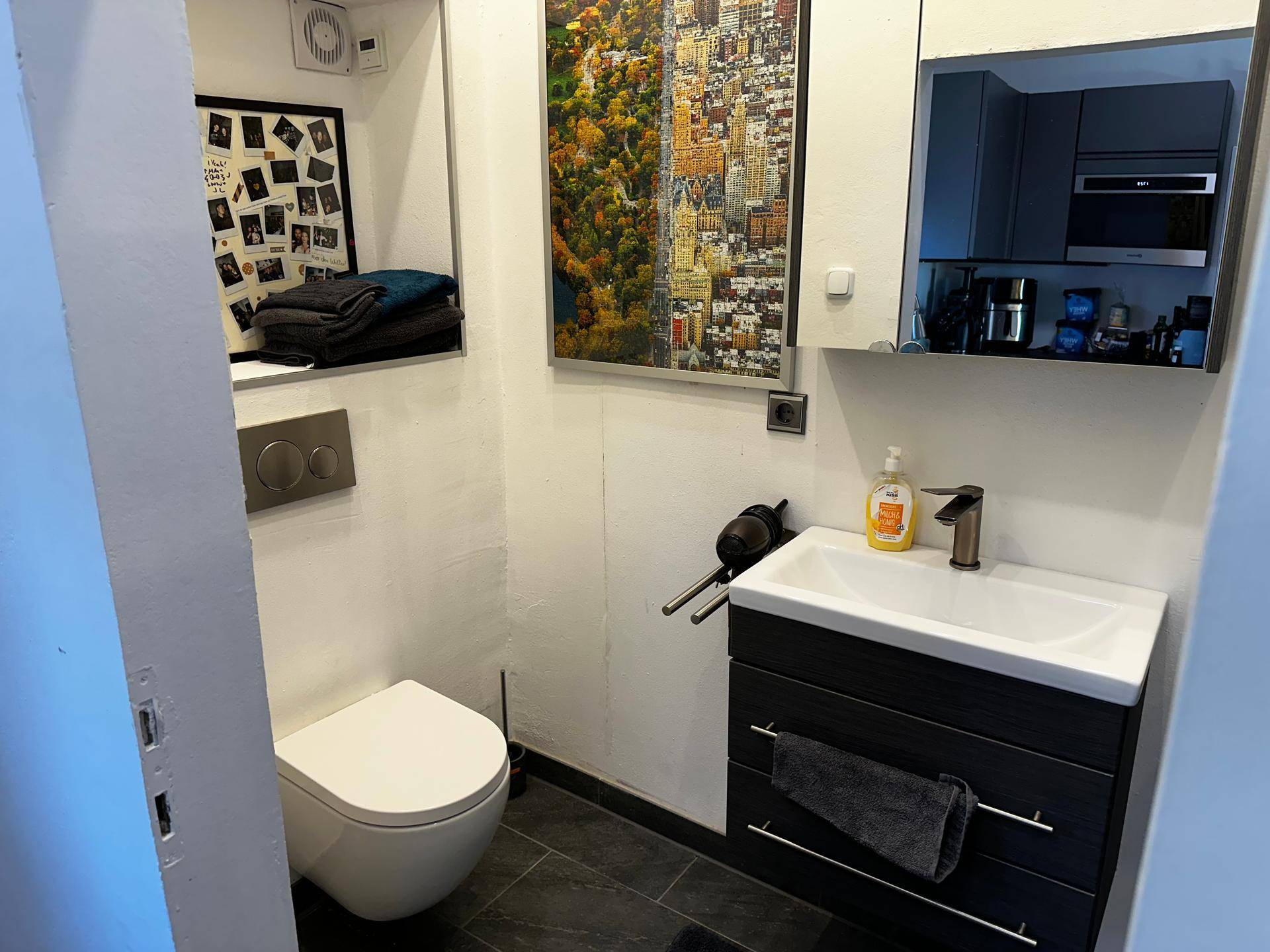 Kompaktes Gäste-WC mit modernem Waschbecken, Wand-WC und dunklen Fliesen.