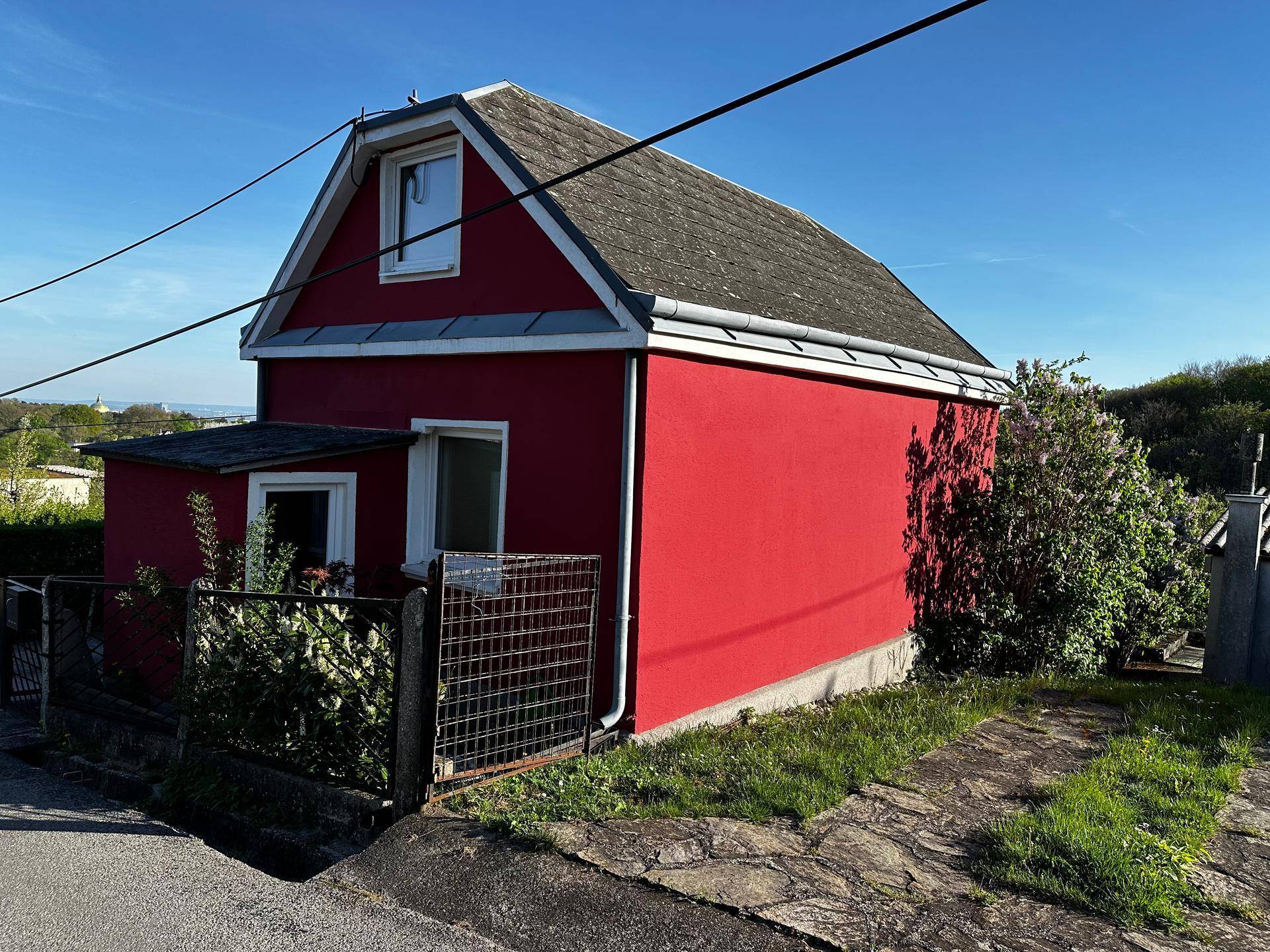 Rotes Haus mit Satteldach und kleiner Anbau, umgeben von Grünflächen.
