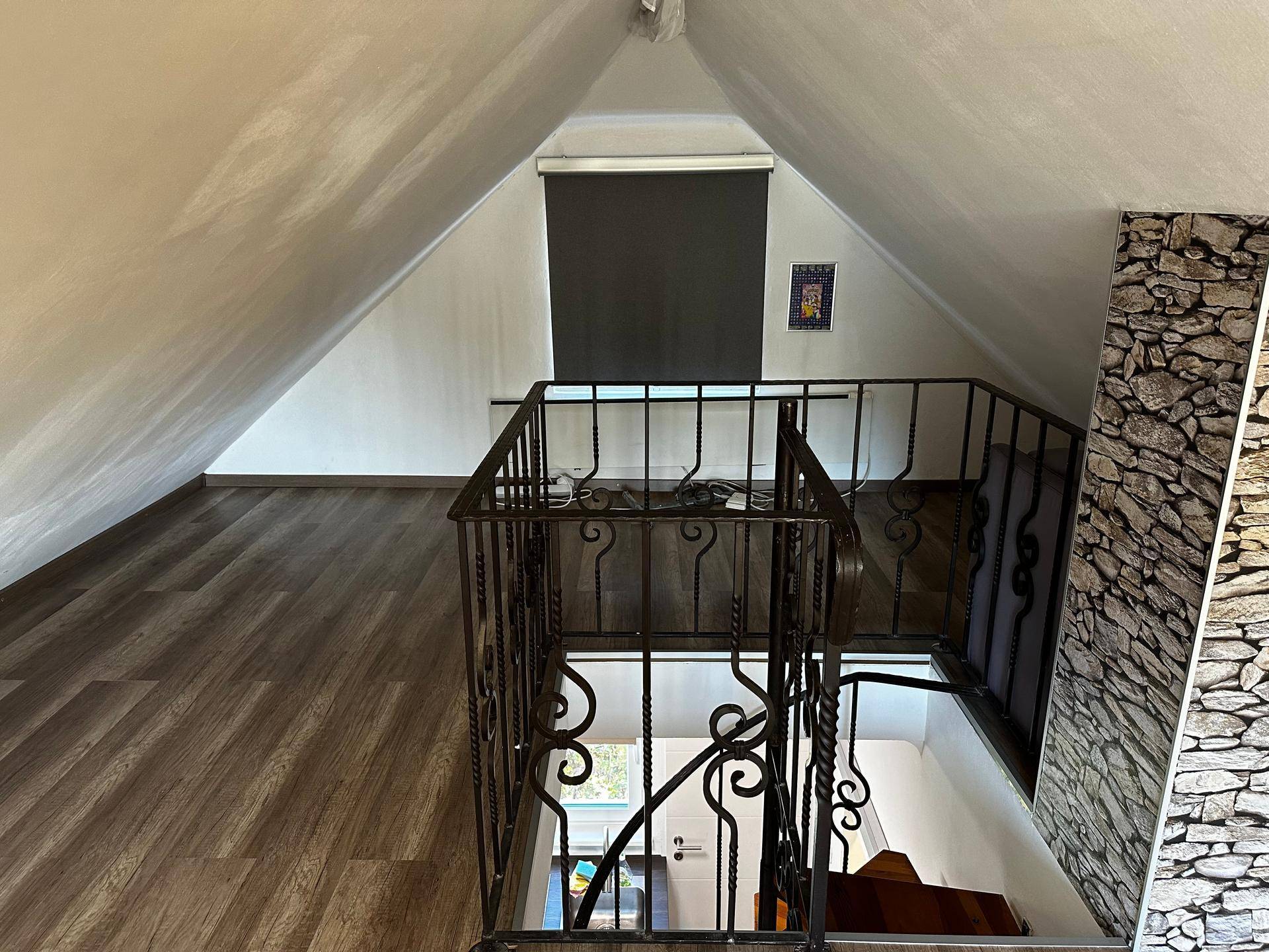 Dachgeschossbereich mit Holzboden und schmiedeeisernem Geländer zur Treppe.