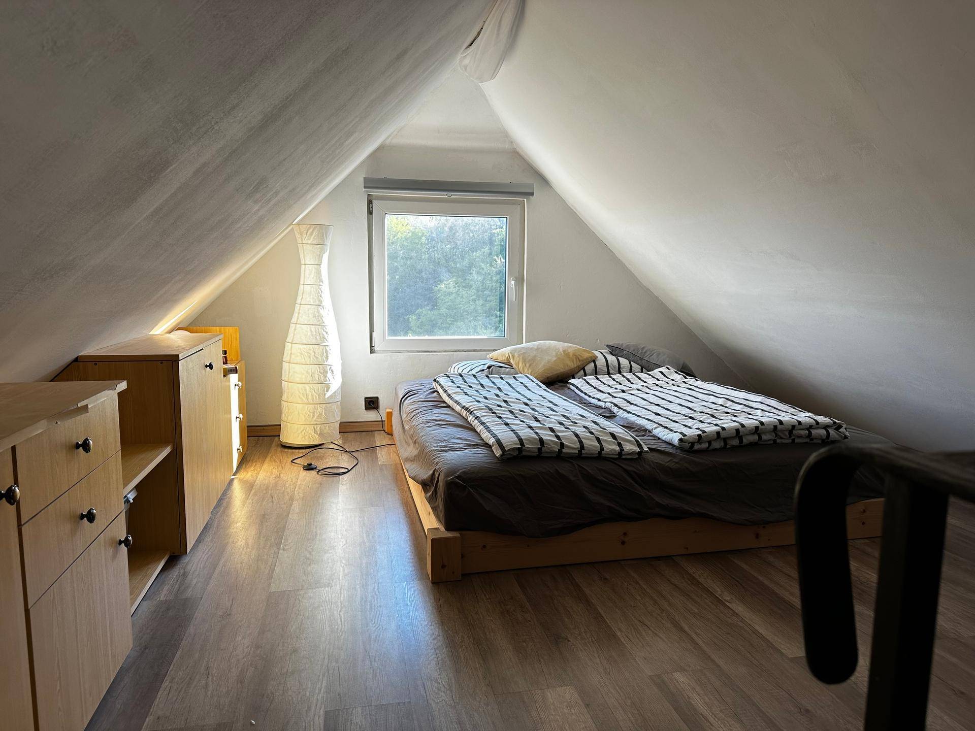 Gemütliches Schlafzimmer im Dachgeschoss mit Holzboden und schrägen Wänden.