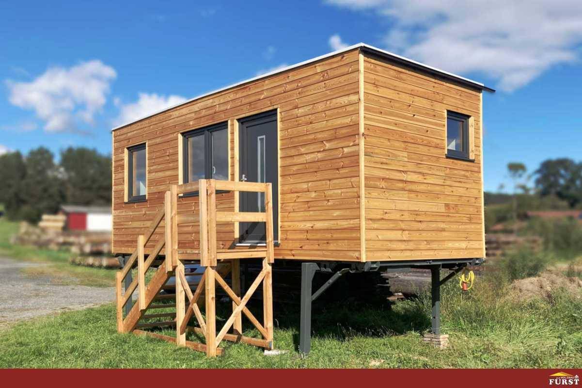 Freistehendes Tiny House mit Holzverkleidung und erhöhter Holztreppe in ländlicher Umgebung.