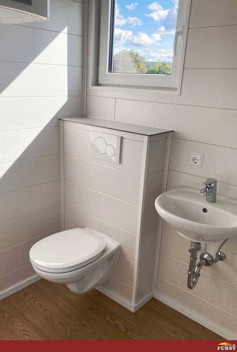 Wandhängendes WC mit integriertem Spülkasten und kleinem Waschbecken im hellen Bad.