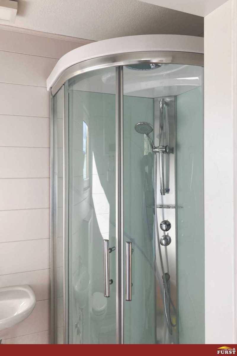 Moderne Duschkabine mit Glaswänden und integrierter Duscharmatur in hellem Bad.