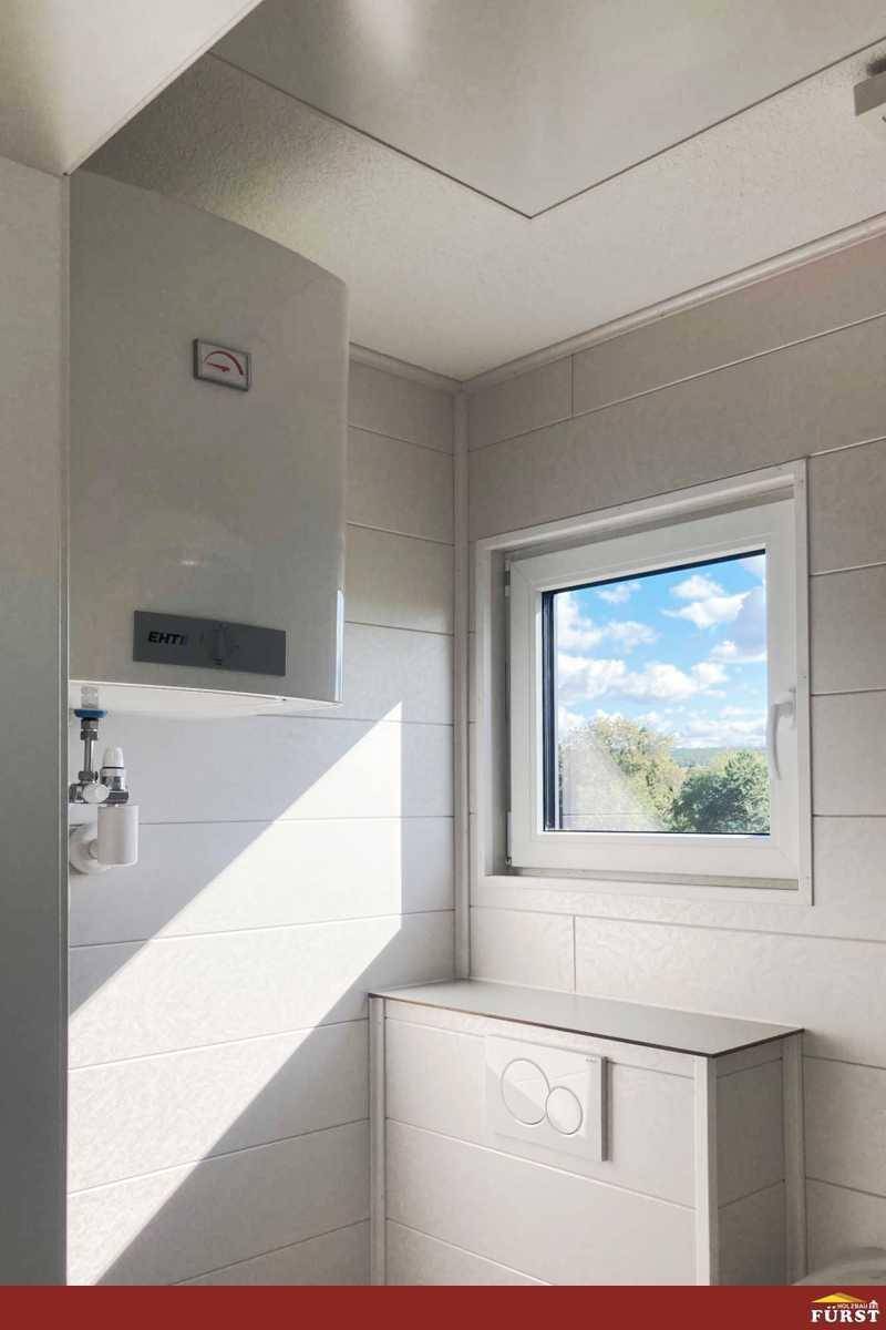 Helles Badezimmer mit Fenster, Wandheizung und verdecktem Spülkasten.