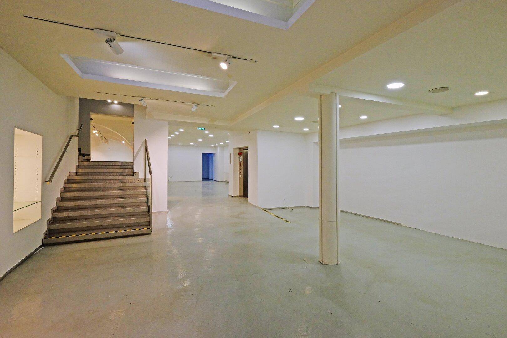 Geräumiger, heller Innenraum mit Treppe, Säulen und Einbaustrahlern, ideal für verschiedene Nutzungen.