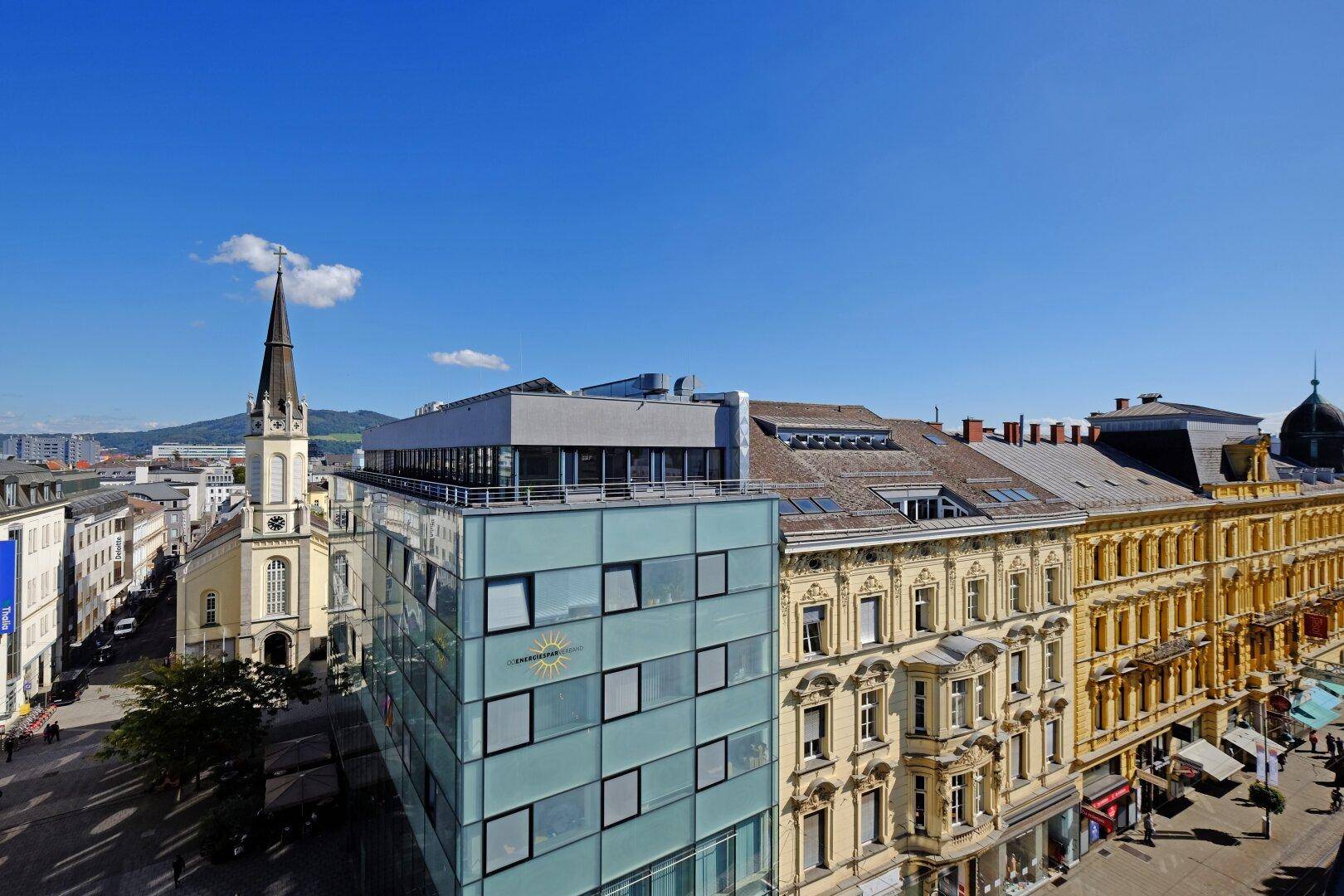 Weitblick über die Stadt mit einer Kirche, historischen Fassaden und modernen Bauten an einem sonnigen Tag.