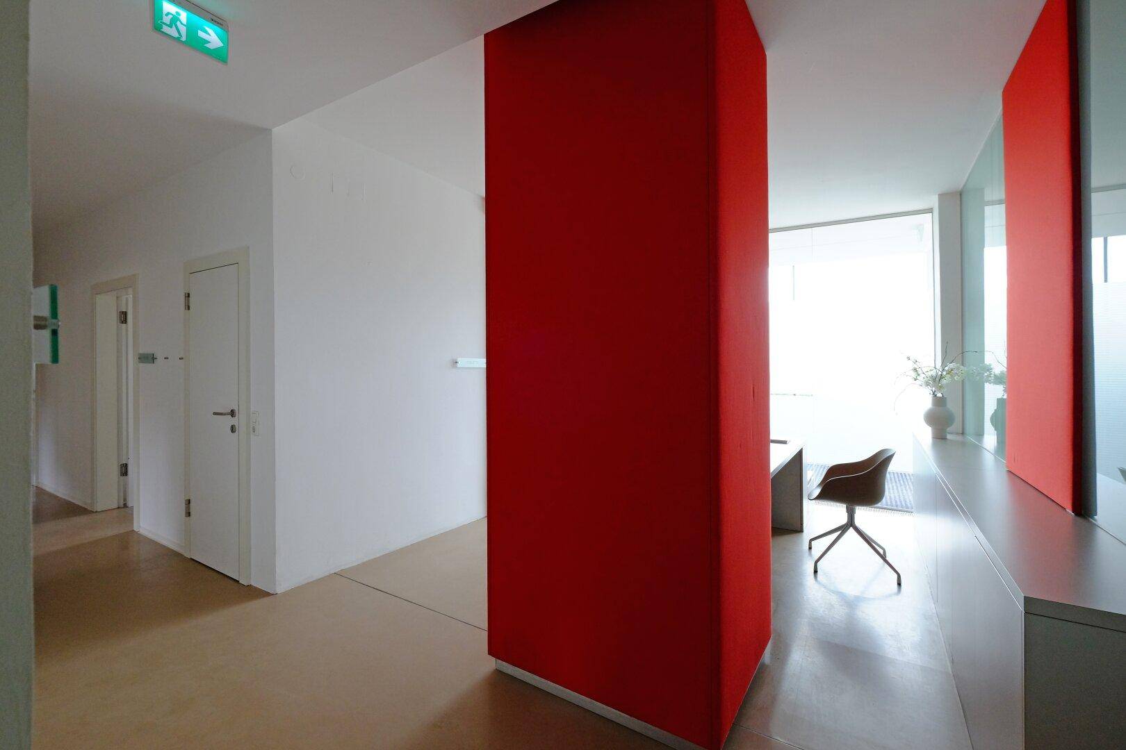 Heller Flur mit roter Säule und Blick in einen lichtdurchfluteten Bürobereich.