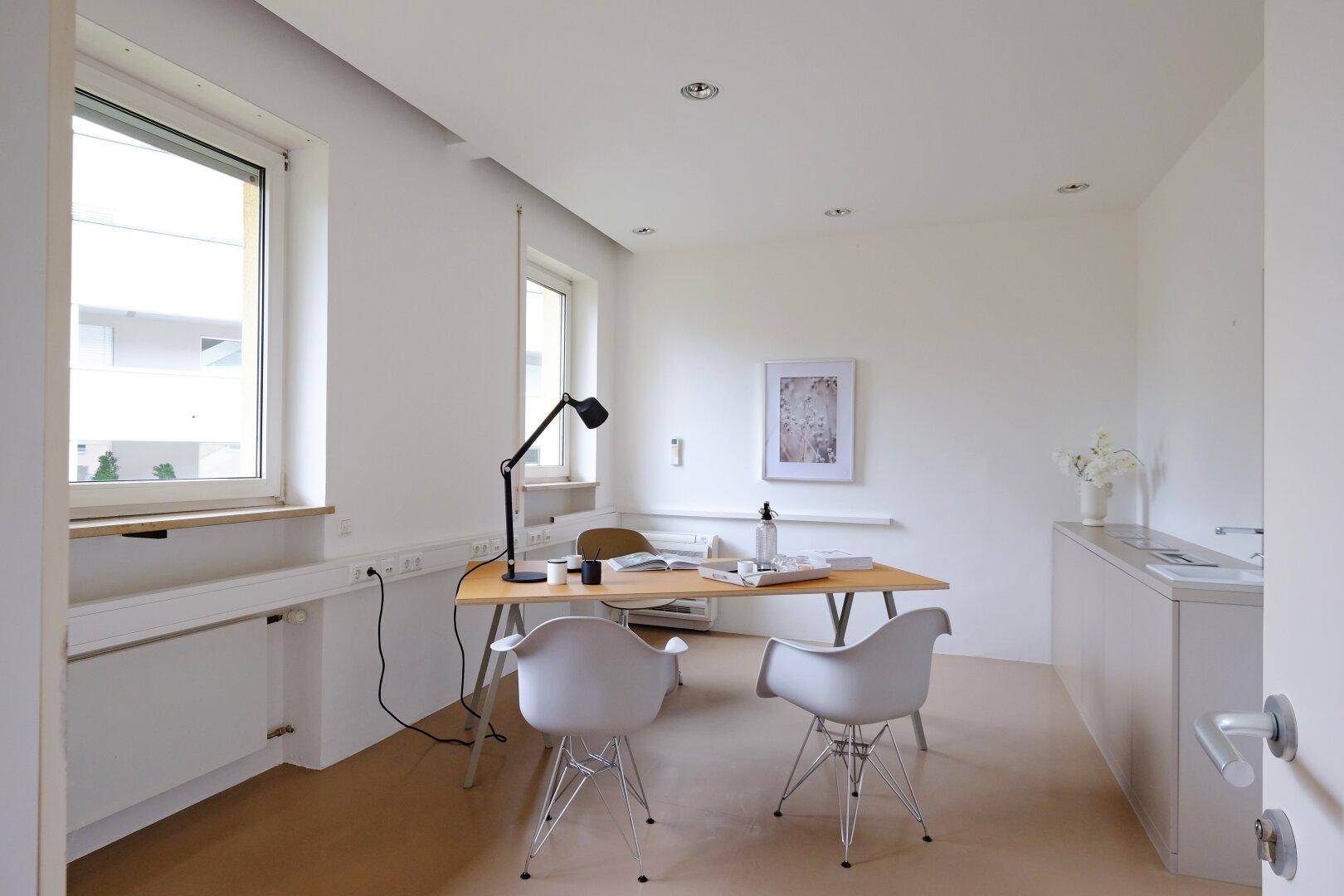 Helles Büro mit Schreibtisch, modernen Stühlen und großen Fenstern für viel Tageslicht.