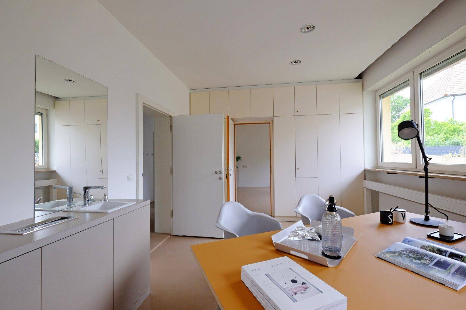Büro mit Schreibtisch, Einbauschränken und einem Waschbeckenbereich mit Spiegel.