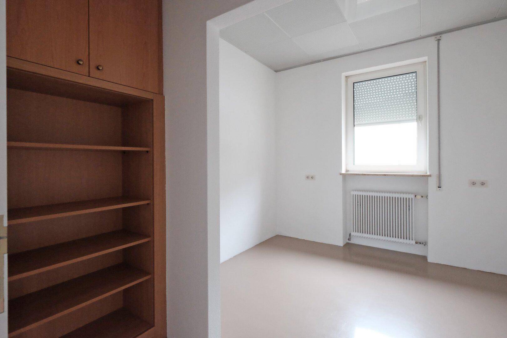 Büro mit Einbauregalen aus Holz und Fenster mit Rollladen.