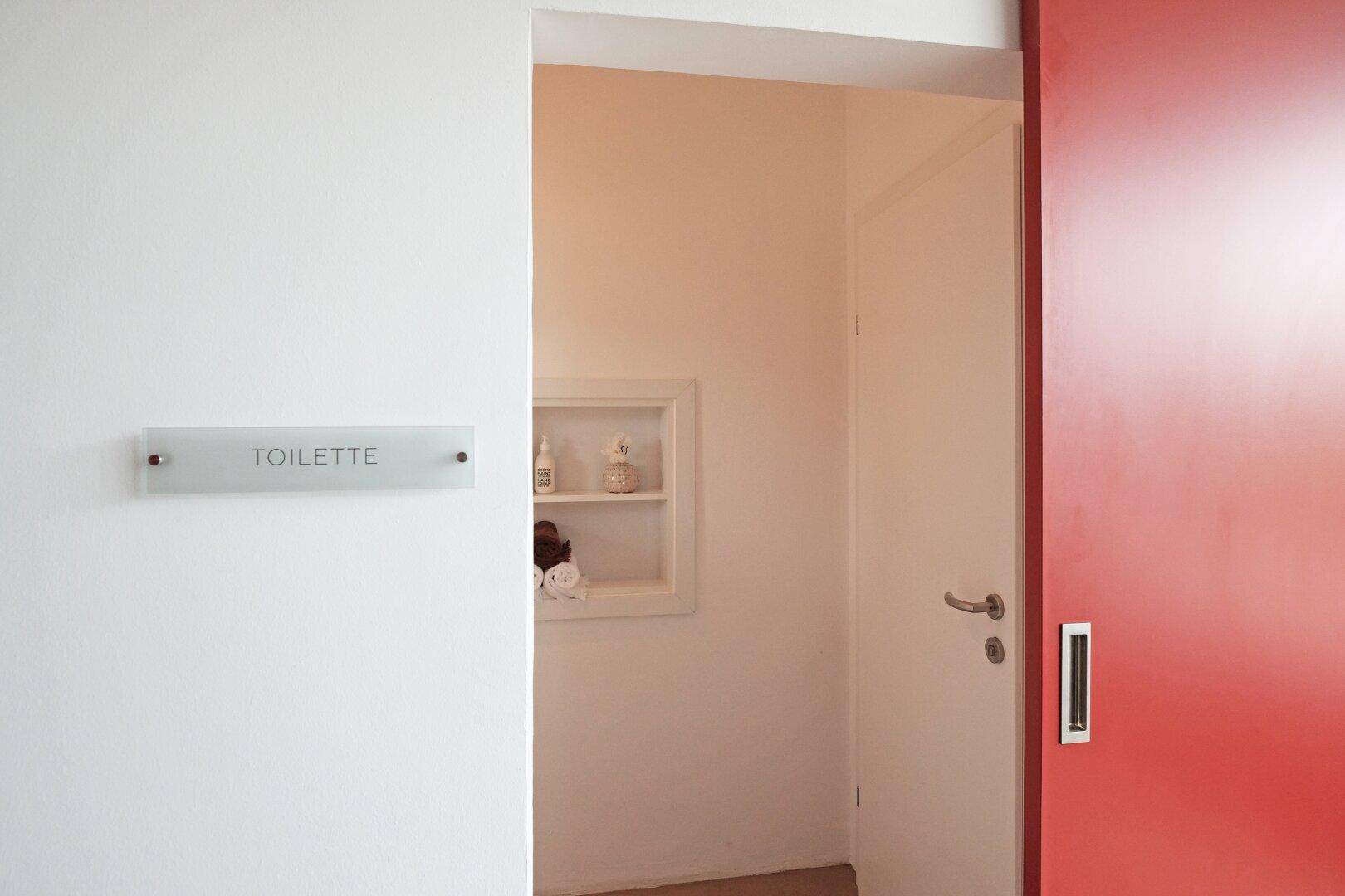 Eingang zu einer Toilette mit Schiebetür und integrierten Wandregalen.