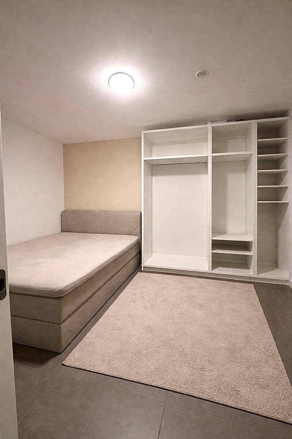 Schlafzimmer mit Bett, offenem Kleiderschrank und Fliesenboden.