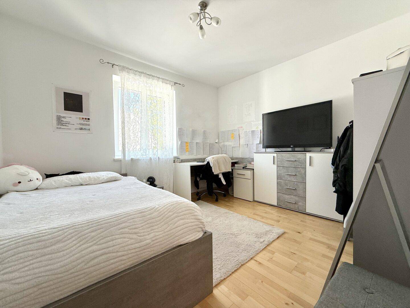 Helles Schlafzimmer mit Holzboden, Schreibtisch und großem Fenster für viel Tageslicht.