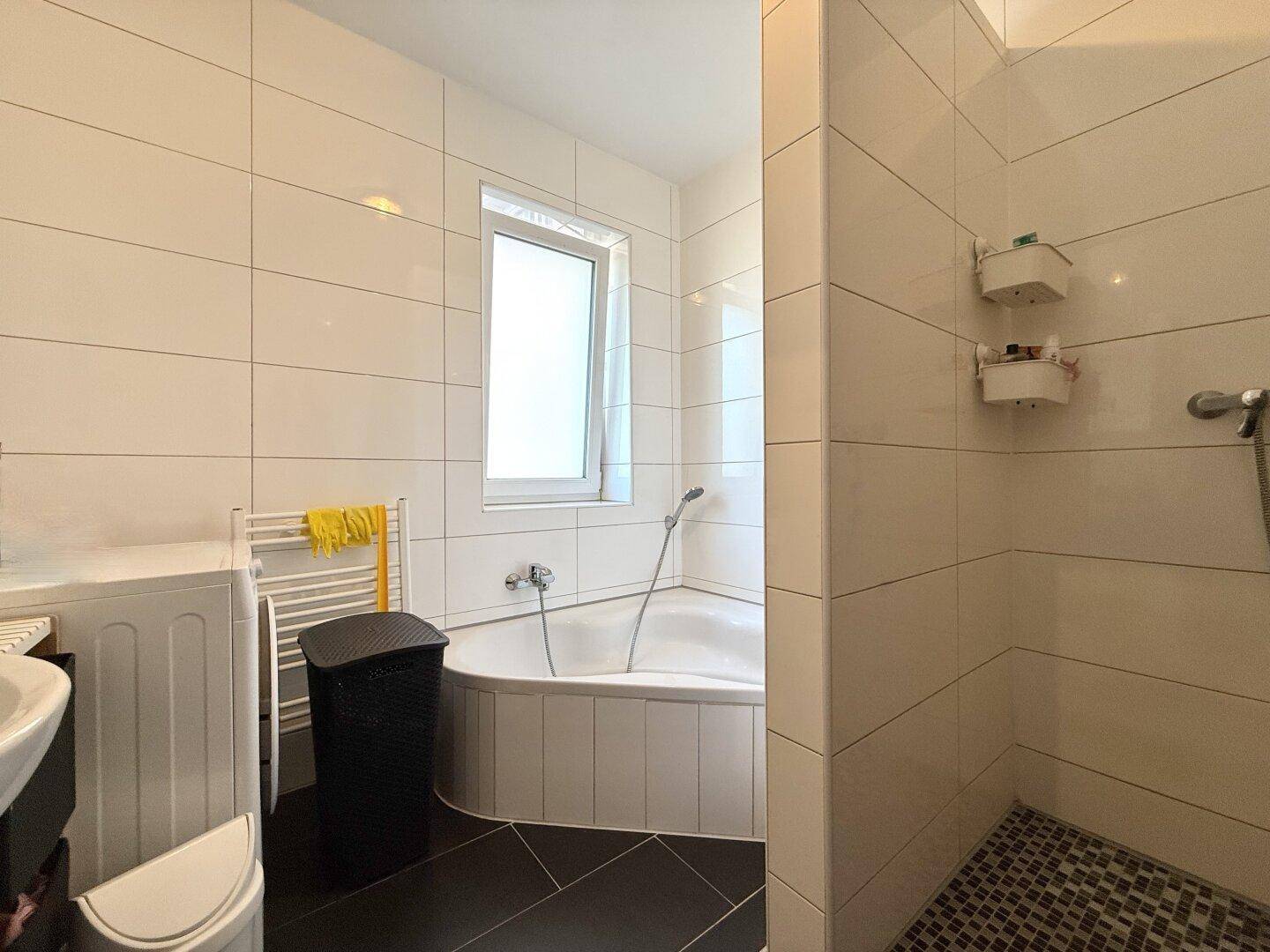 Modernes Badezimmer mit Eckbadewanne, separater Dusche und Fenster für natürliche Belüftung.