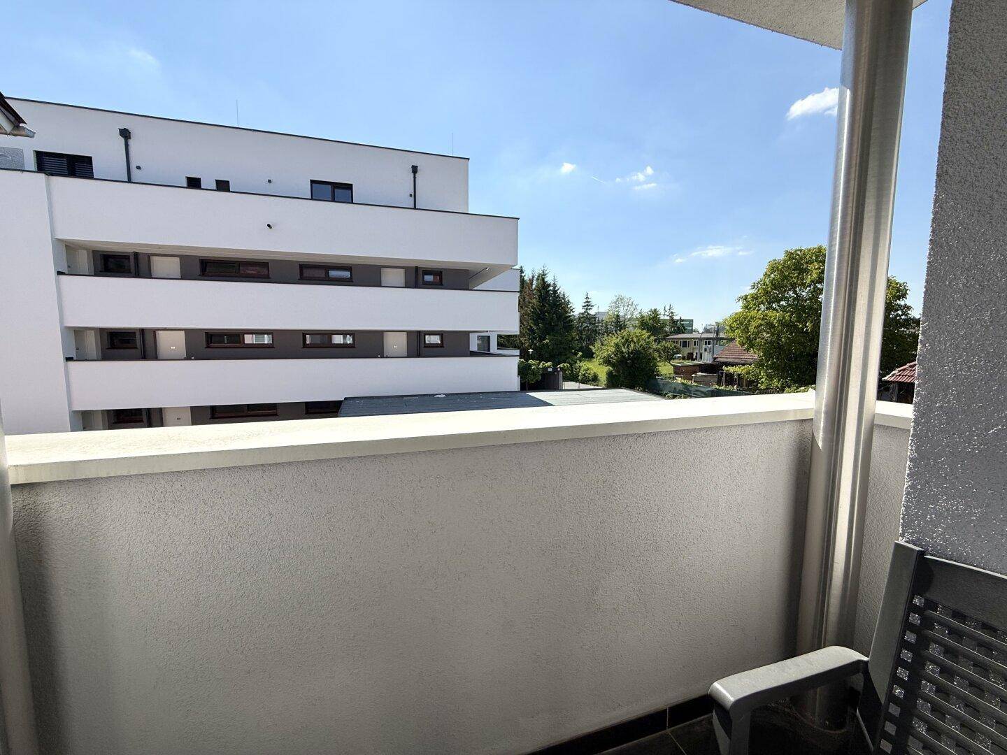 Balkon mit Blick auf moderne Gebäude und grüne Umgebung unter blauem Himmel.