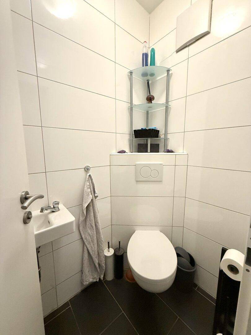 Kleines Gäste-WC mit wandhängendem WC, Waschbecken und modernen Fliesen.