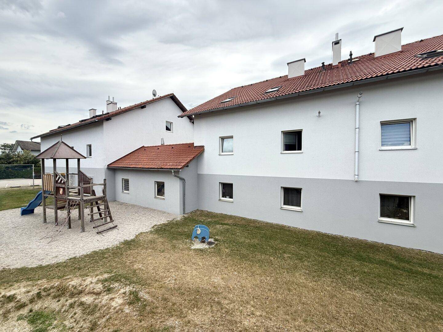 Wohngebäude mit Spielplatz und Rasenfläche an einem bewölkten Tag, ideal für Familien.