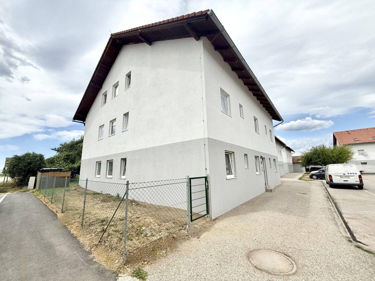 Seitenansicht eines Wohnhauses mit Zaun und Kiesweg unter bewölktem Himmel.