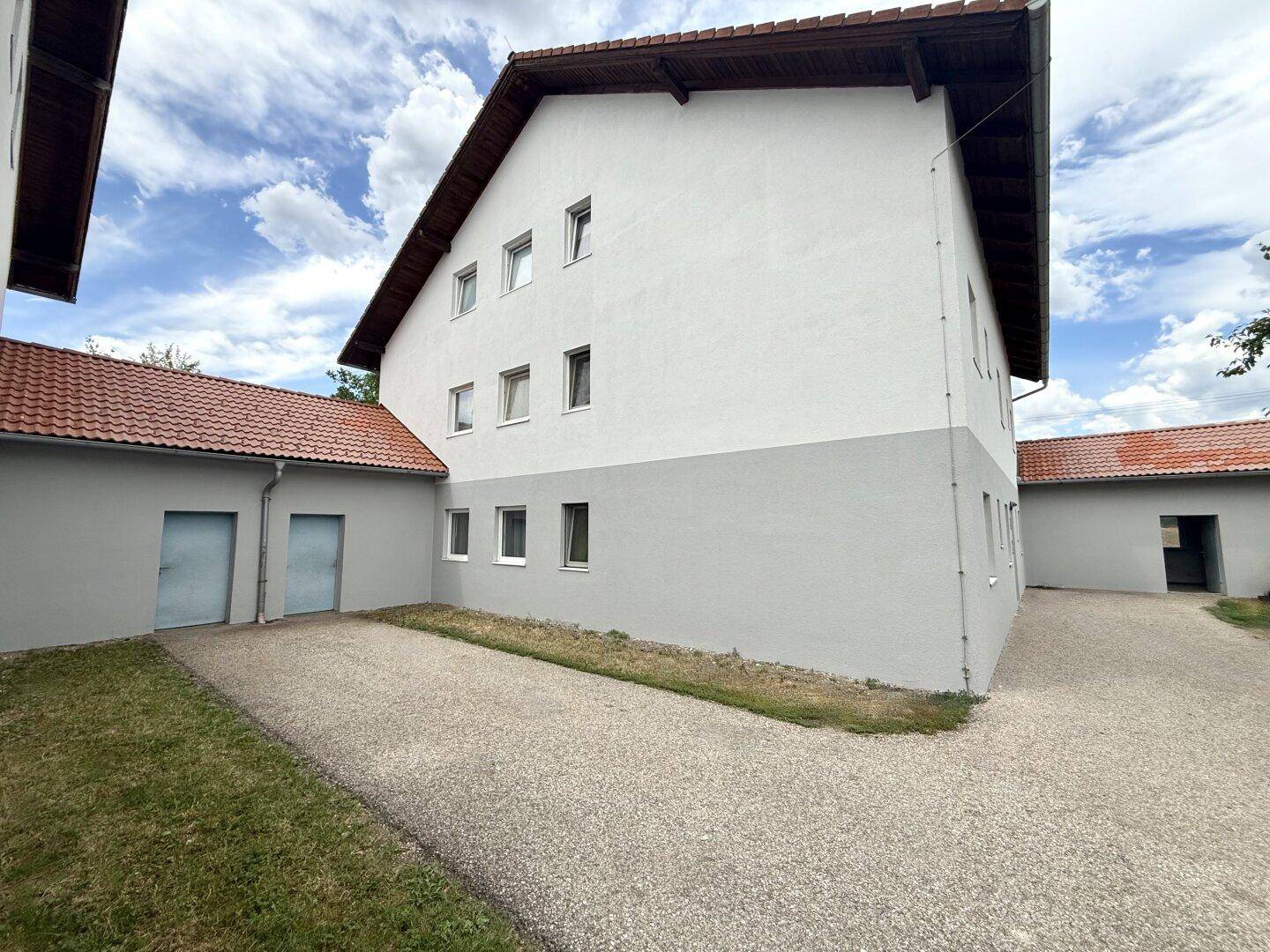 Seitenansicht eines Wohnhauses mit angrenzendem Nebengebäude und Kiesfläche.