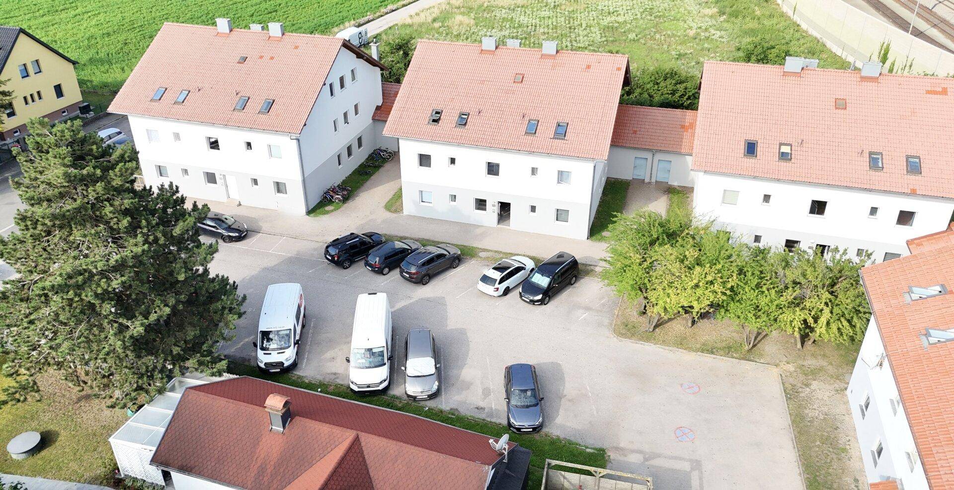 Luftaufnahme einer Wohnsiedlung mit mehreren Häusern und Parkplätzen unter blauem Himmel.