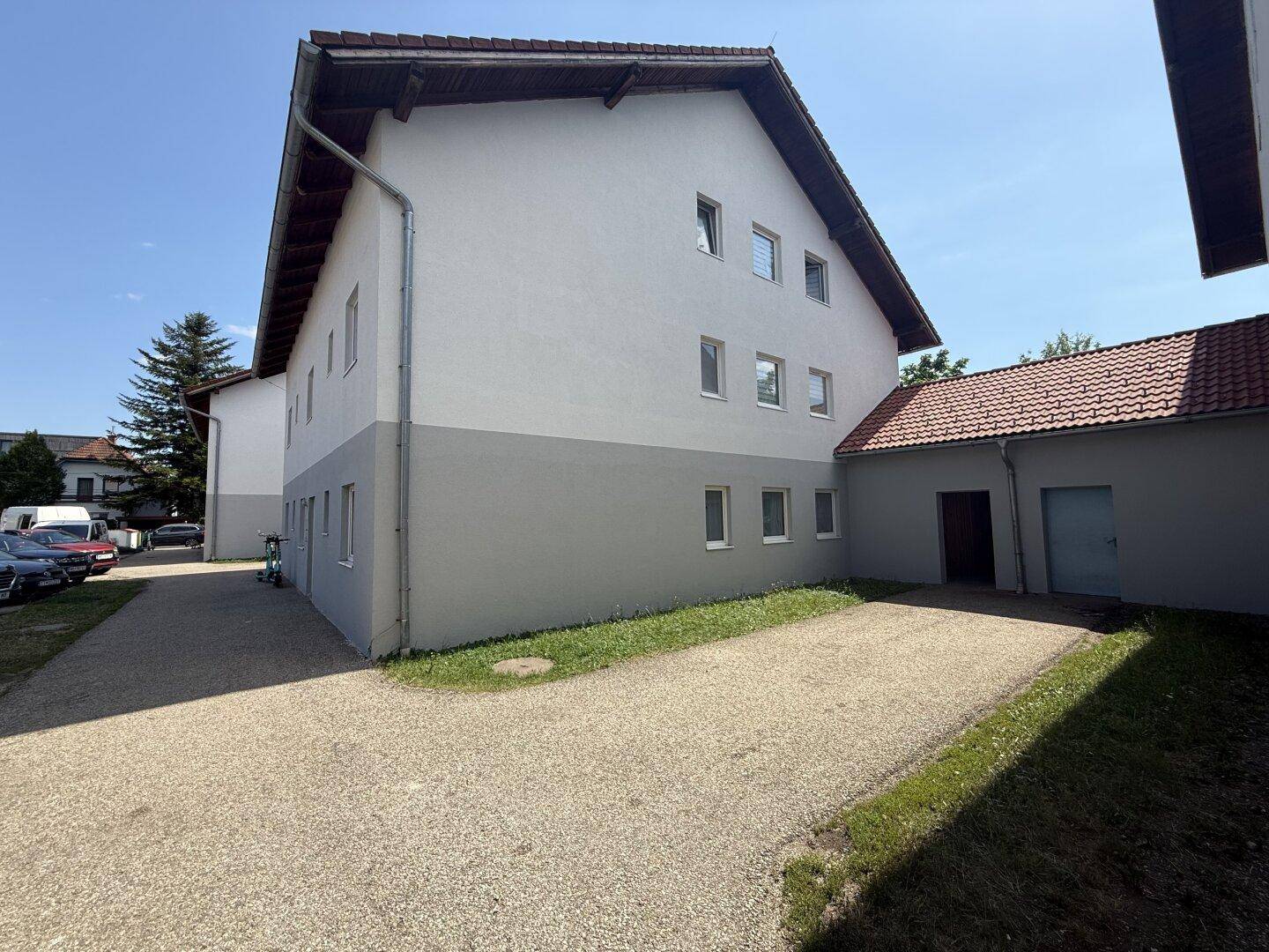 Seitenansicht eines Wohnhauses mit weiß-grauer Fassade und Kiesfläche unter blauem Himmel.