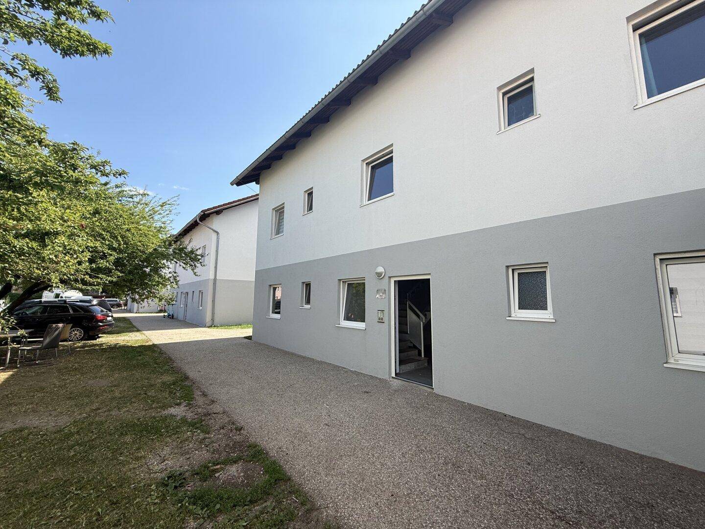 Eingangsbereich eines Wohnhauses mit weiß-grauer Fassade, Kiesweg und umliegender Grünfläche.