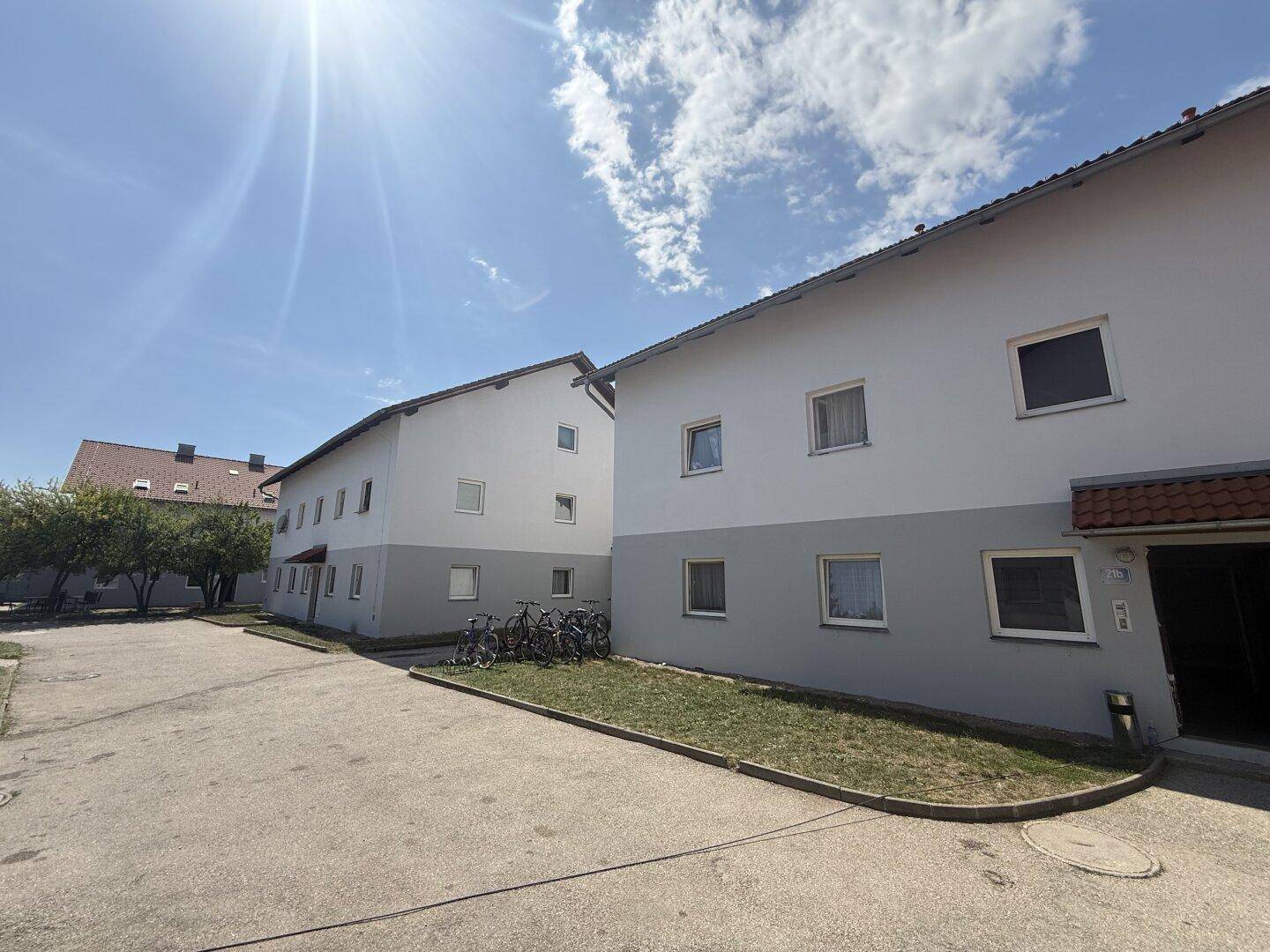 Mehrere Wohngebäude mit weiß-grauer Fassade und Fahrrädern vor dem Eingangsbereich.