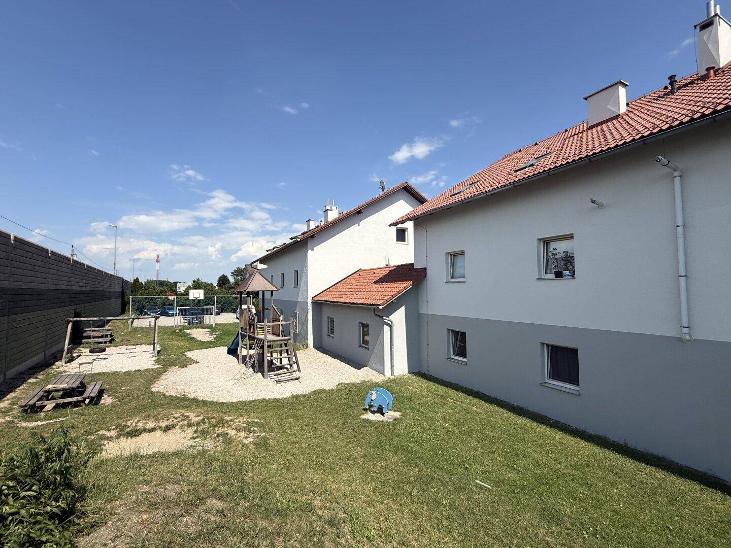 Spielplatz mit Rutsche und Sandkasten neben den Wohngebäuden unter blauem Himmel.