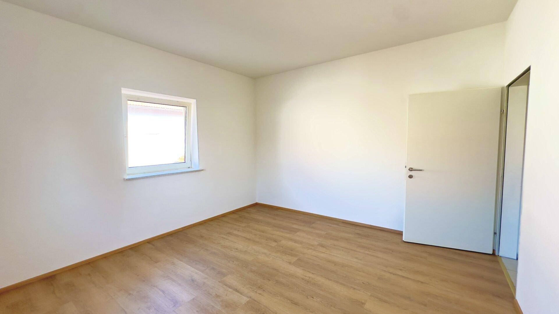 Geräumiges, helles Zimmer mit Laminatboden und weiß gestrichenen Wänden, bereit zur Einrichtung.