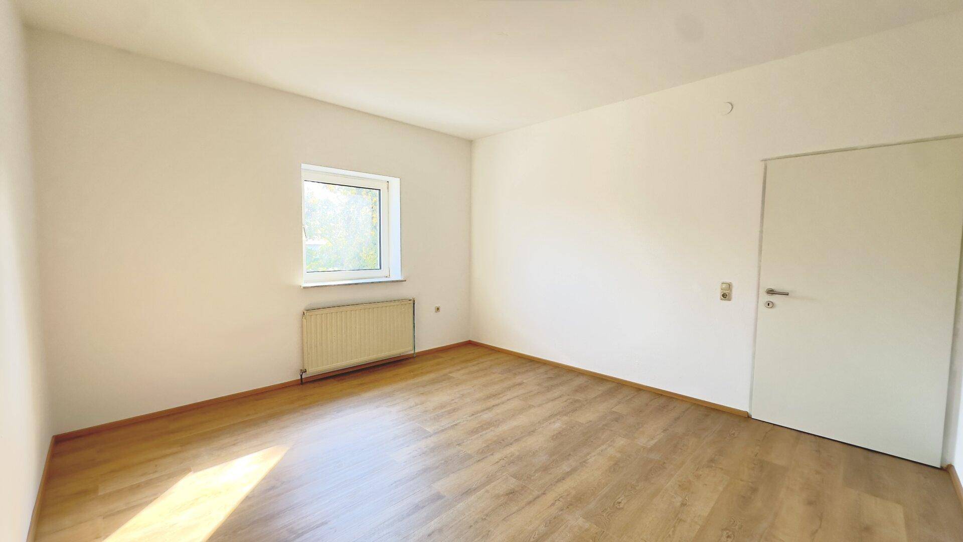 Freundliches, unmöbliertes Zimmer mit Laminatboden, weißen Wänden und einem Fenster für viel Tageslicht.