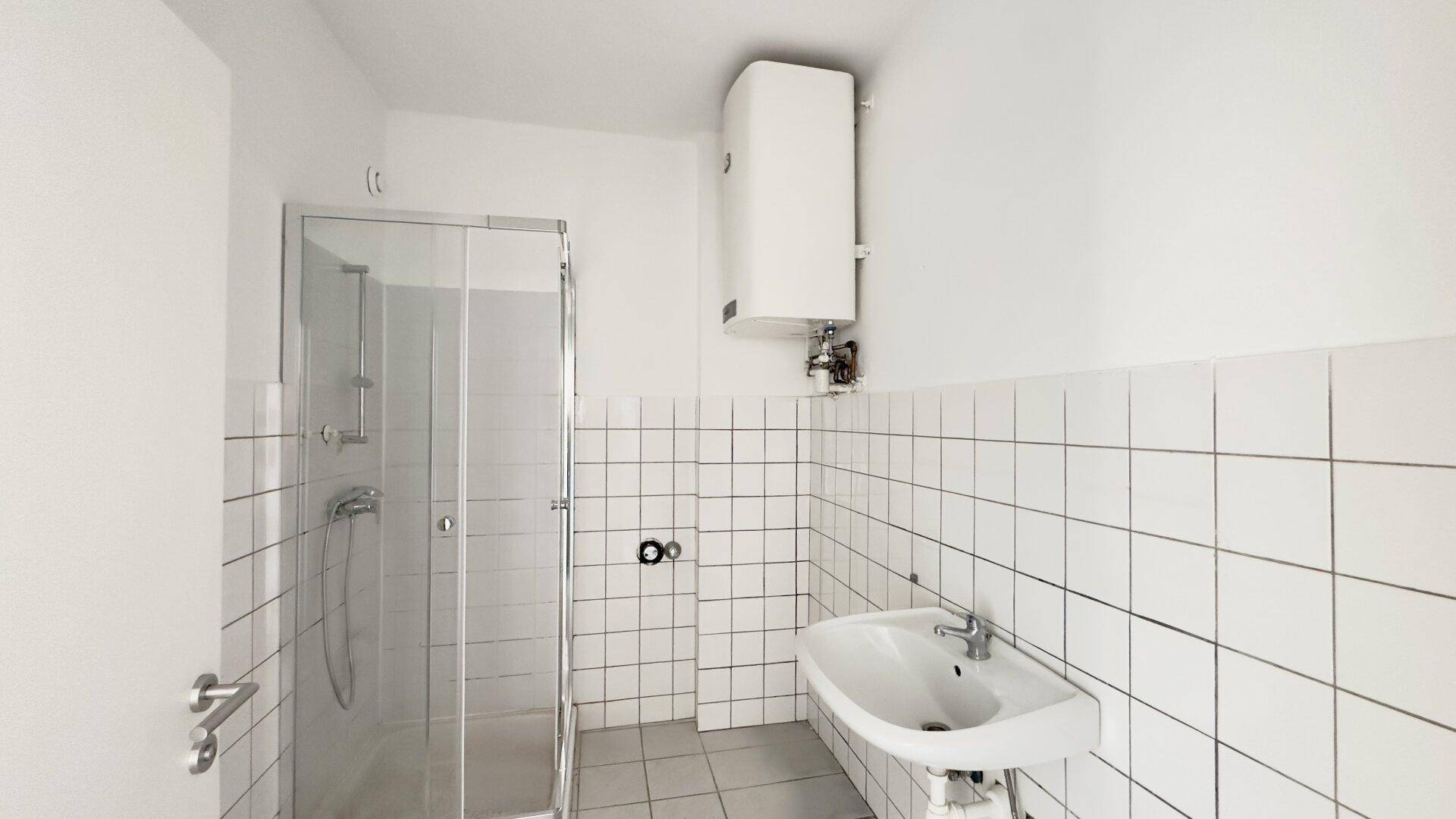 Modernes Badezimmer mit weiß gefliesten Wänden, Duschkabine und einem Waschbecken.
