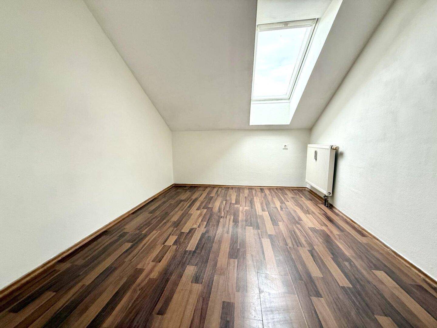 Geräumiger Dachgeschossraum mit viel Tageslicht durch das große Dachfenster.