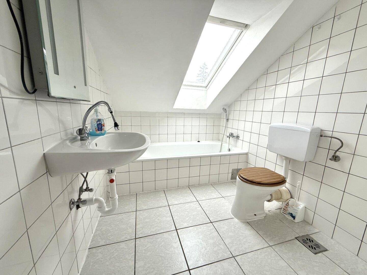 Helles Badezimmer im Dachgeschoss mit Badewanne, WC, Waschbecken und Dachfenster.