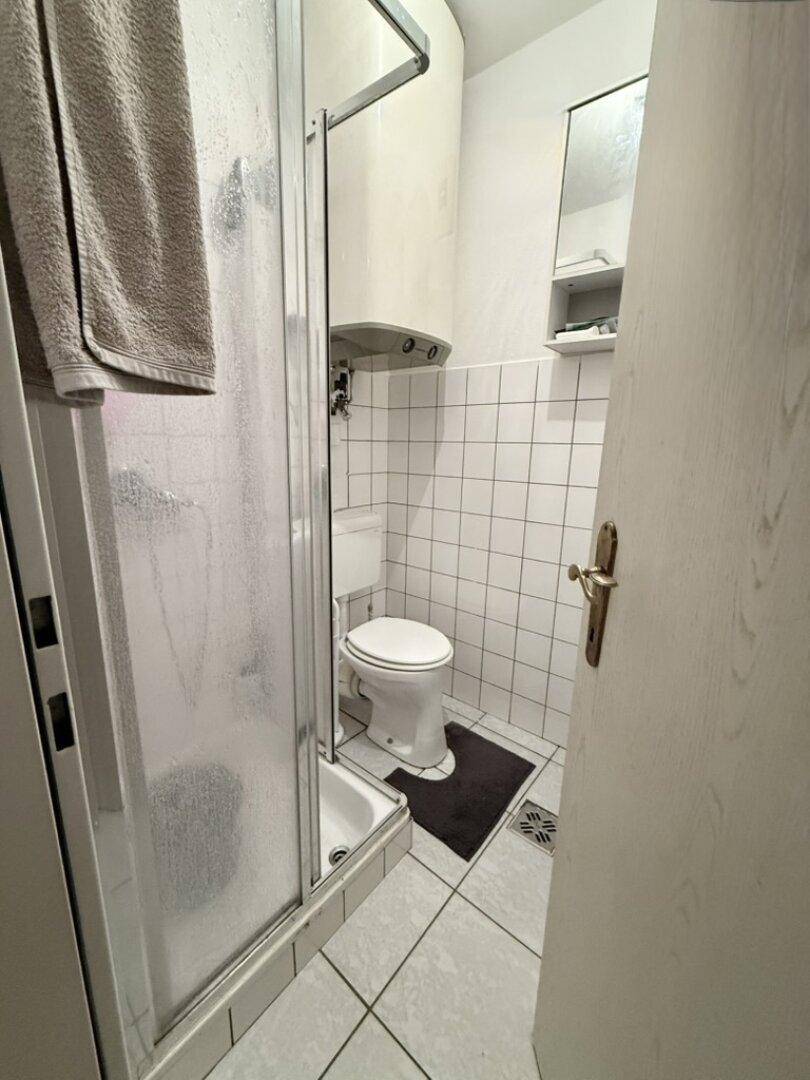 Kleines Badezimmer mit Duschkabine, Toilette und weiß gefliesten Wänden.