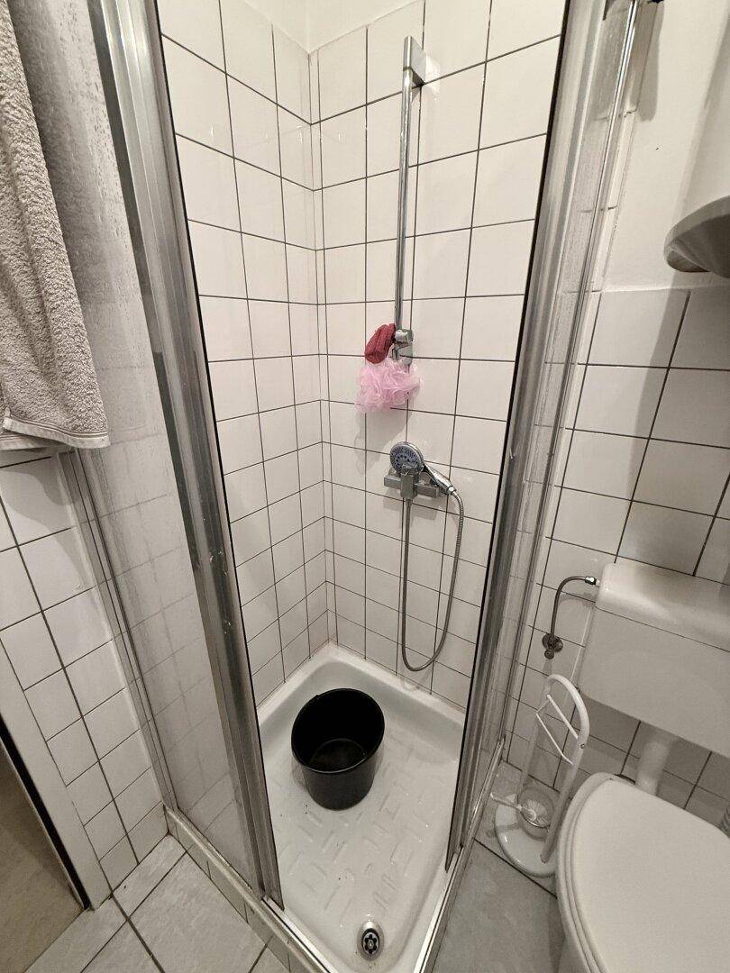 Duschkabine im Badezimmer mit weißen Fliesen und einfacher Ausstattung.