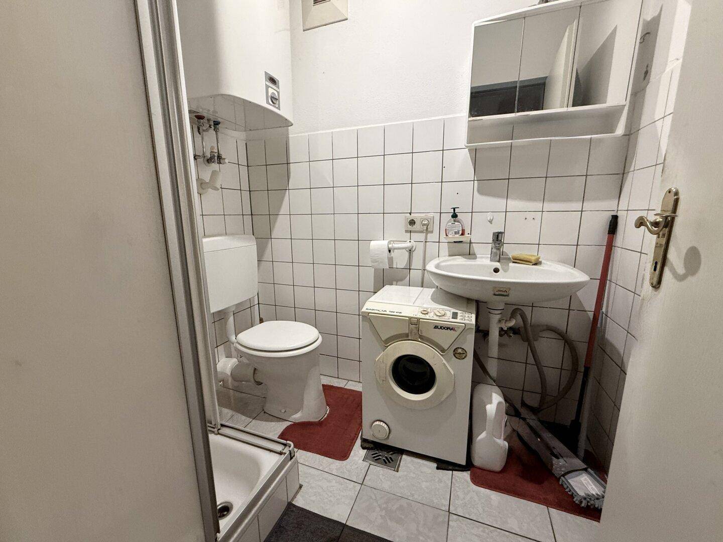 Kleines Badezimmer mit Dusche, WC, Waschbecken und Waschmaschine.