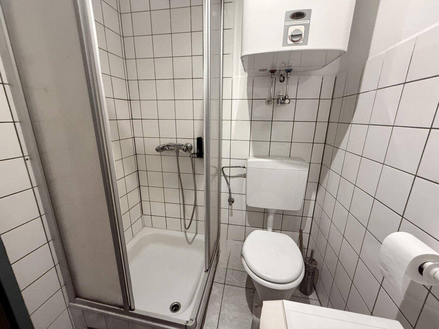 Badezimmer mit Duschkabine, Toilette und weiß gefliesten Wänden.