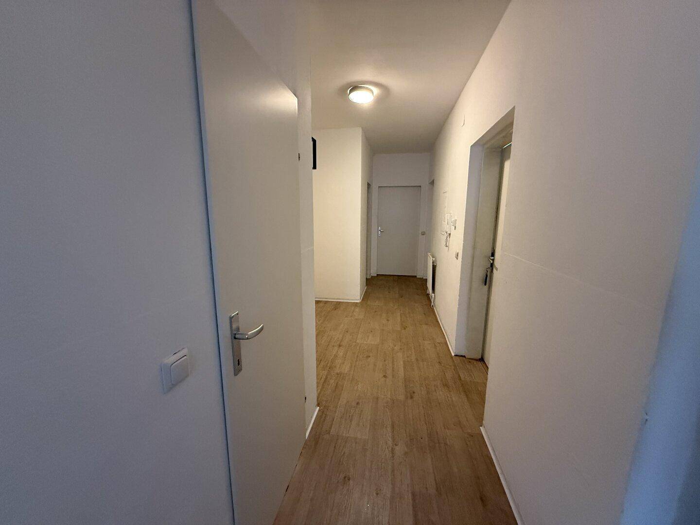 Heller Flur mit Laminatboden und weißen Wänden, der zu verschiedenen Räumen führt.