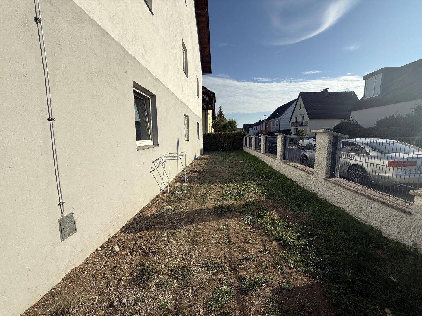 Seitenansicht des Gebäudes mit einem schmalen Grasstreifen und Blick auf die Nachbarschaft.