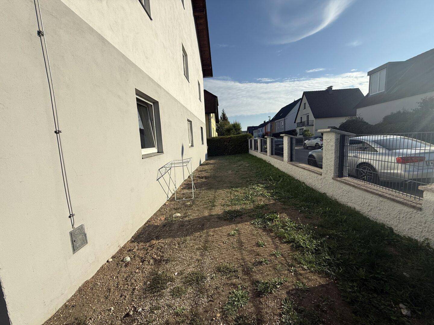Seitenansicht des Gebäudes mit einem schmalen Grasstreifen und Blick auf die Nachbarschaft.