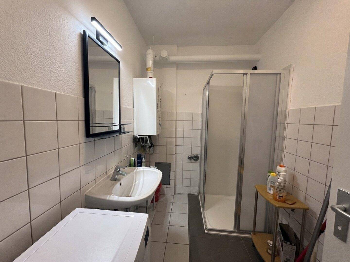 Gefliestes Badezimmer mit Duschkabine, Waschbecken und Warmwasserboiler.