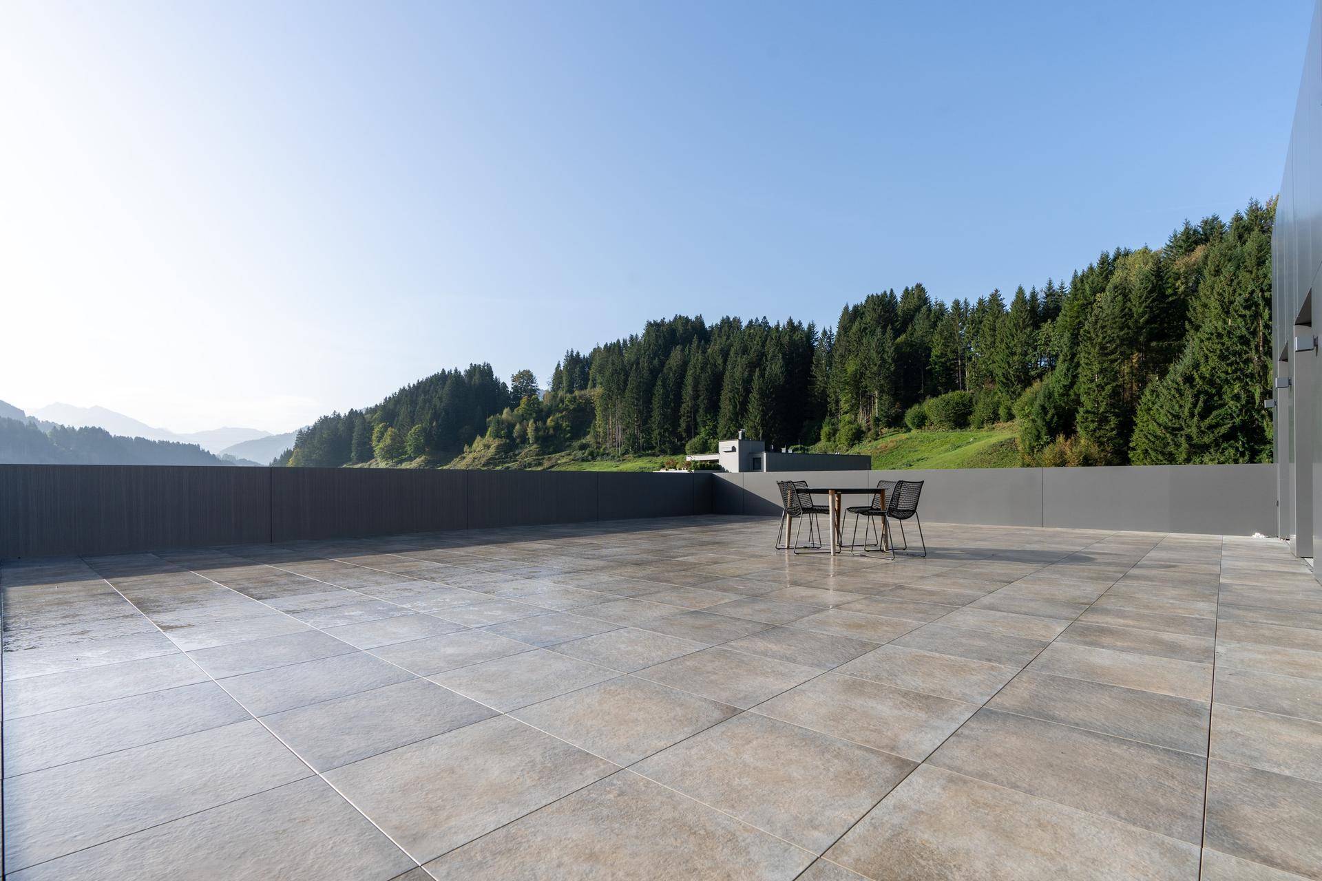 Große, geflieste Dachterrasse mit Sitzgelegenheiten und weitem Blick auf bewaldete Hügel.