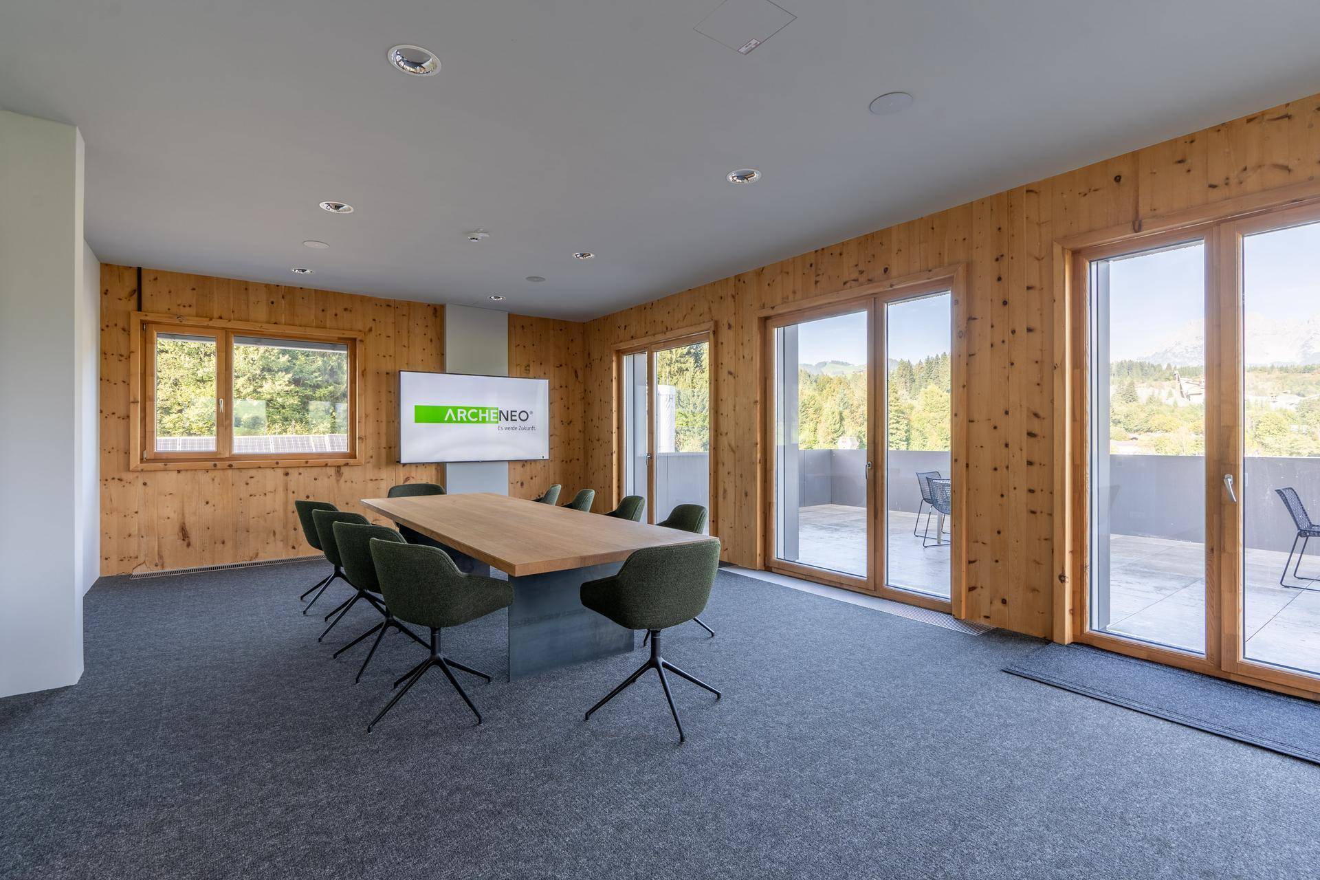 Moderner Konferenzraum mit großem Holztisch, bequemen Stühlen und Zugang zur Terrasse mit Bergblick.