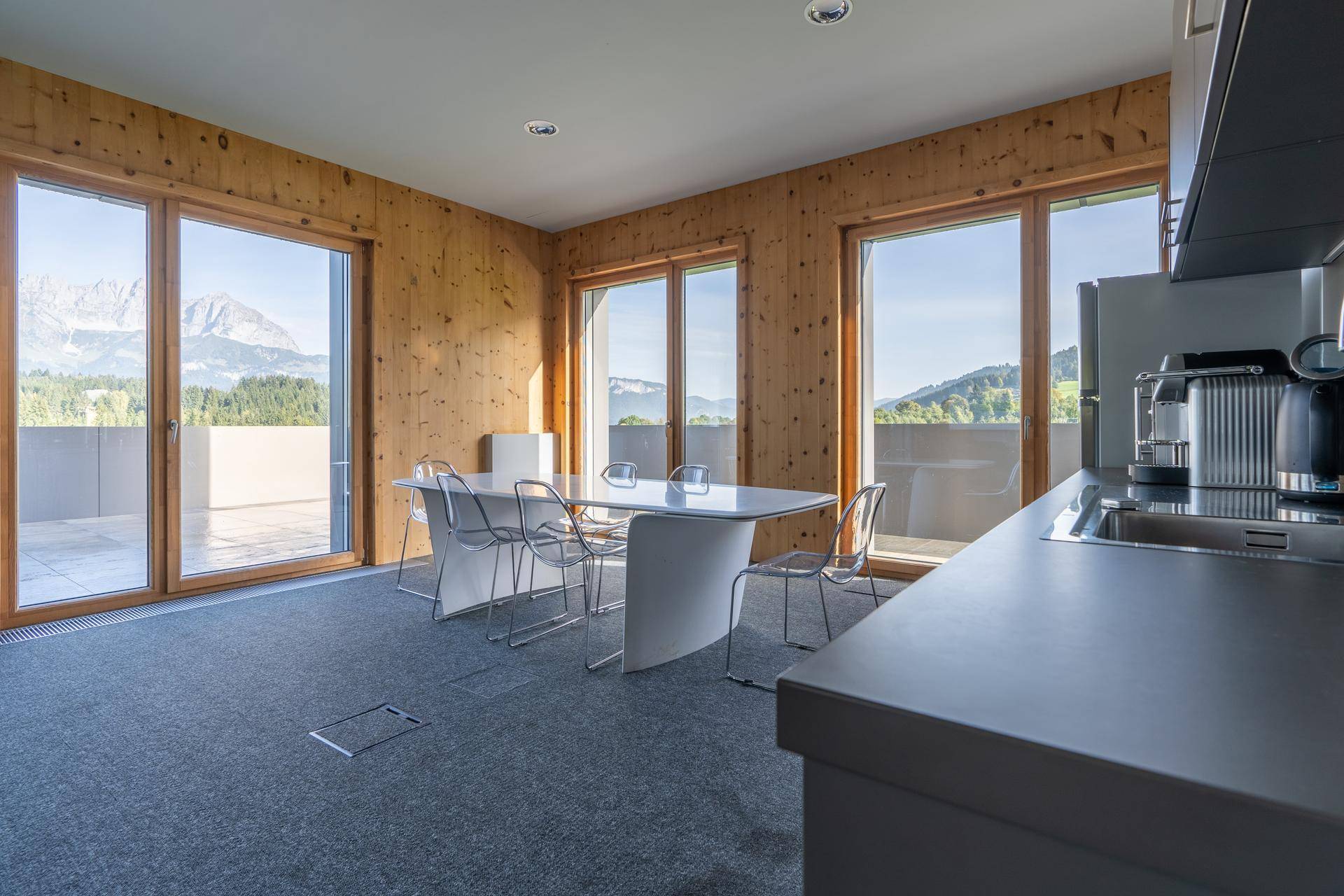 Moderner Essbereich mit Küchenzeile, großen Fenstern und Zugang zur Terrasse mit Bergblick.